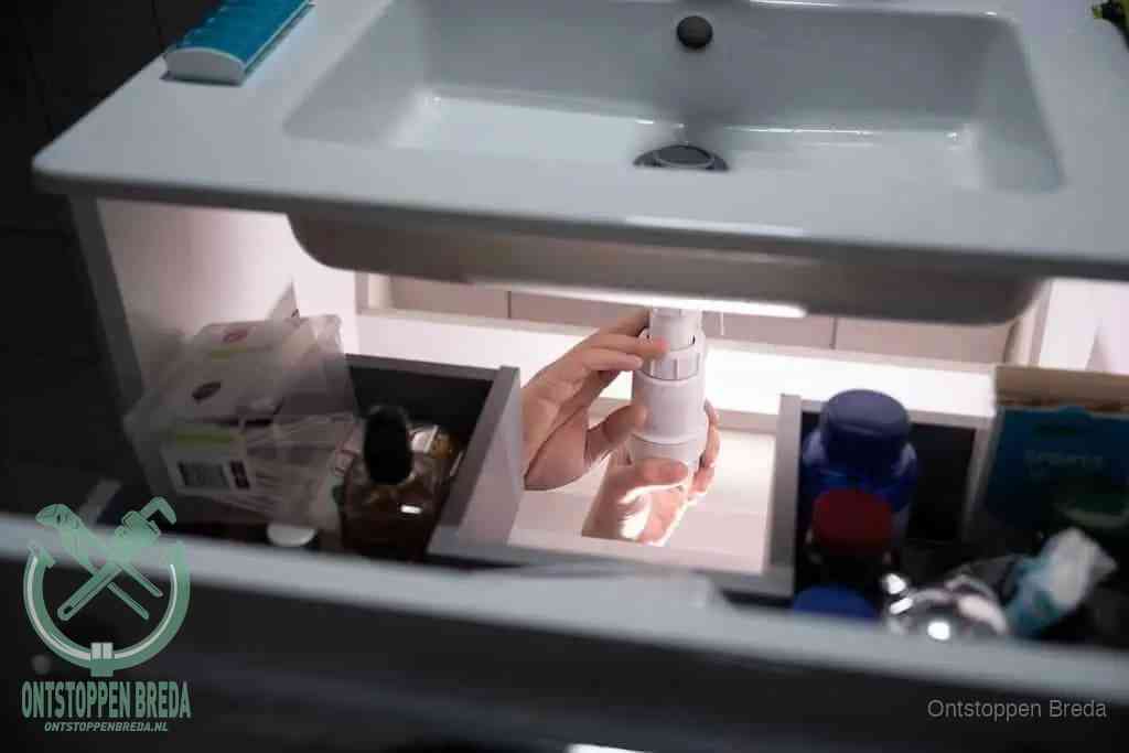 Een pompfles met zeep boven een wastafel, de heet water en afwasmiddel-methode om een vetprop in de afvoer los te maken in Breda