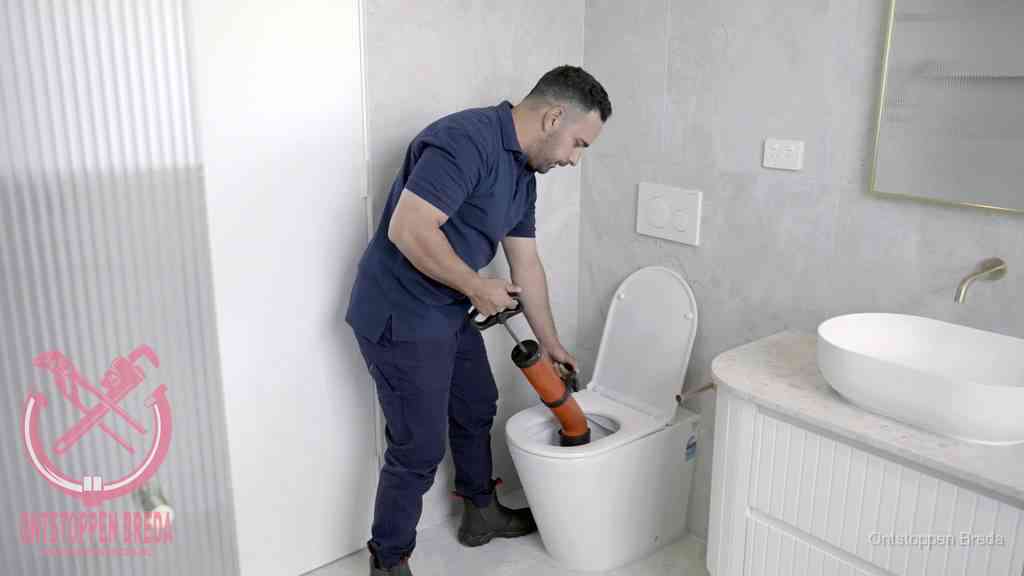 Een monteur buigt over een wandcloset en duwt met de hand een persluchtontstopper in de toiletpot om de verstopping handmatig los te maken in Breda