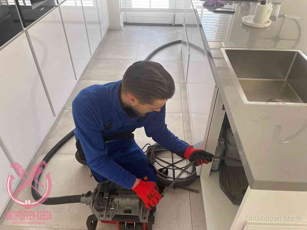 Een monteur ontstopt de keukenafvoer onder de spoelbak met een elektrische veermachine in Breda Een monteur ontstopt de keukenafvoer onder de spoelbak met een elektrische veermachine in Breda