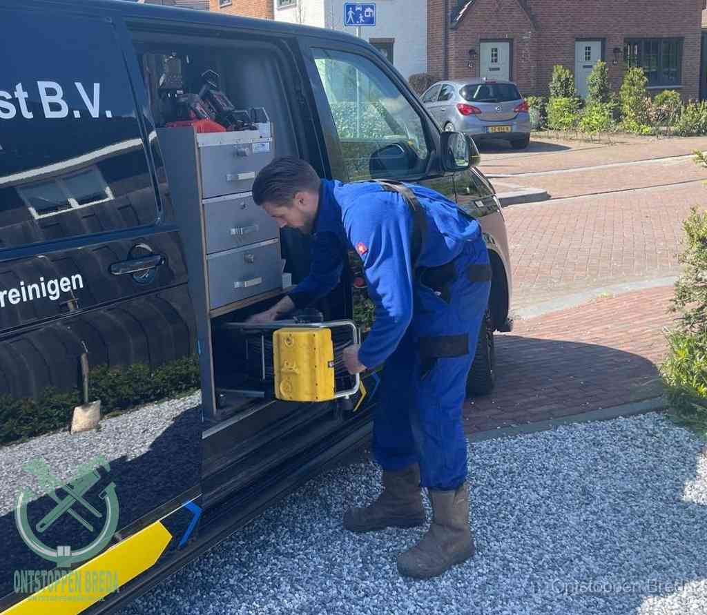 Een monteur pakt buiten op de oprit gereedschap uit de bedrijfsbus, het moment om een professional in te schakelen voor een verstopte afvoer in Breda