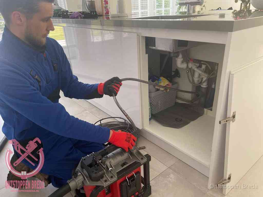 Monteur voert een ontstoppingsveer in de afvoer onder de keuken in Breda Monteur voert een ontstoppingsveer in de afvoer onder de keuken in Breda
