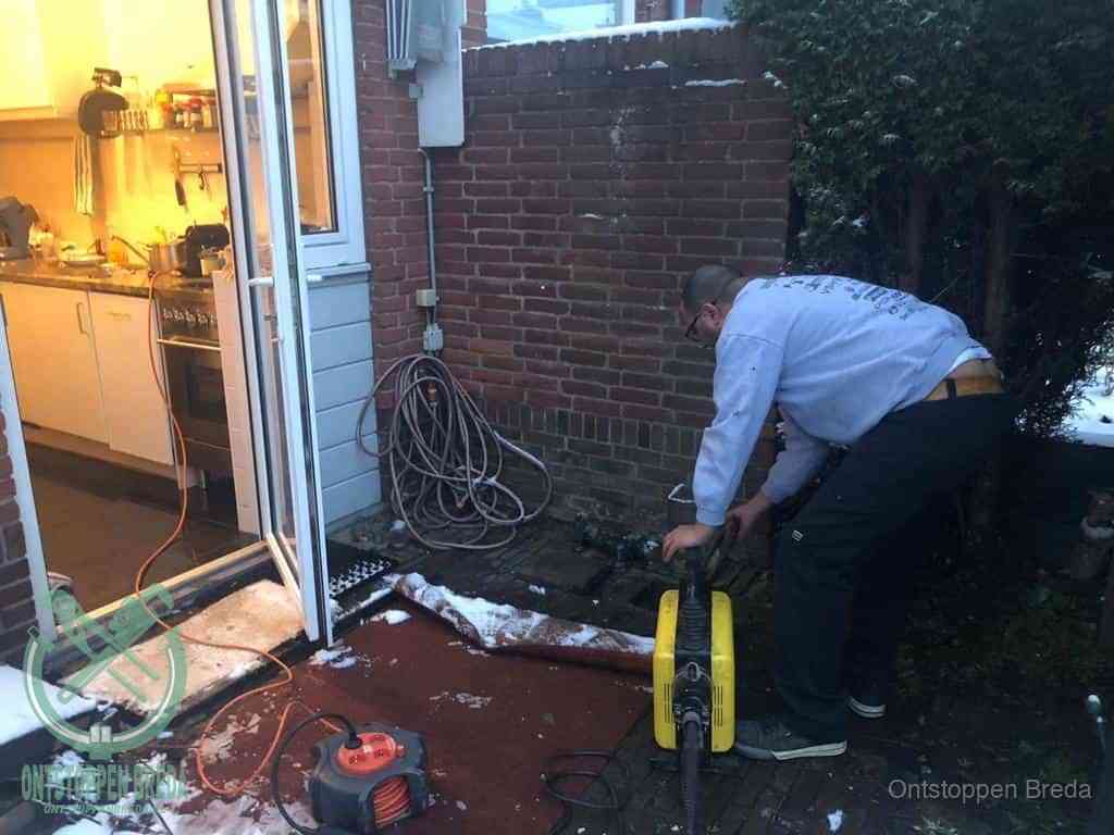 Een monteur werkt buiten bij een open riool-/grondput met een elektrische ontstoppingsmachine om een verborgen afvoerprobleem op te sporen in Breda