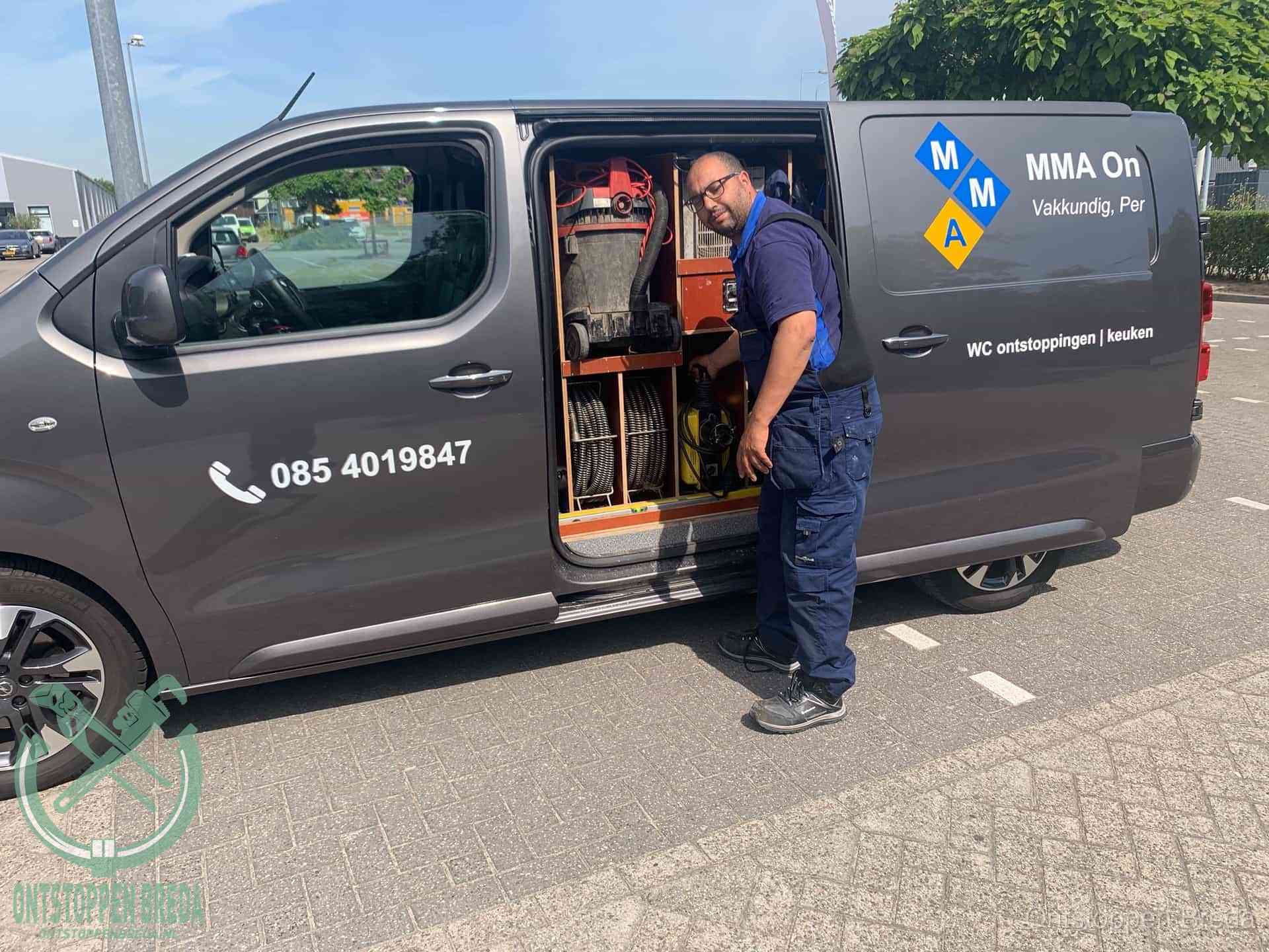 Een monteur bij de open schuifdeur van zijn bedrijfsbus op een parkeerplaats, klaar om de oorzaak van terugkerende afvoerverstoppingen aan te pakken in Breda