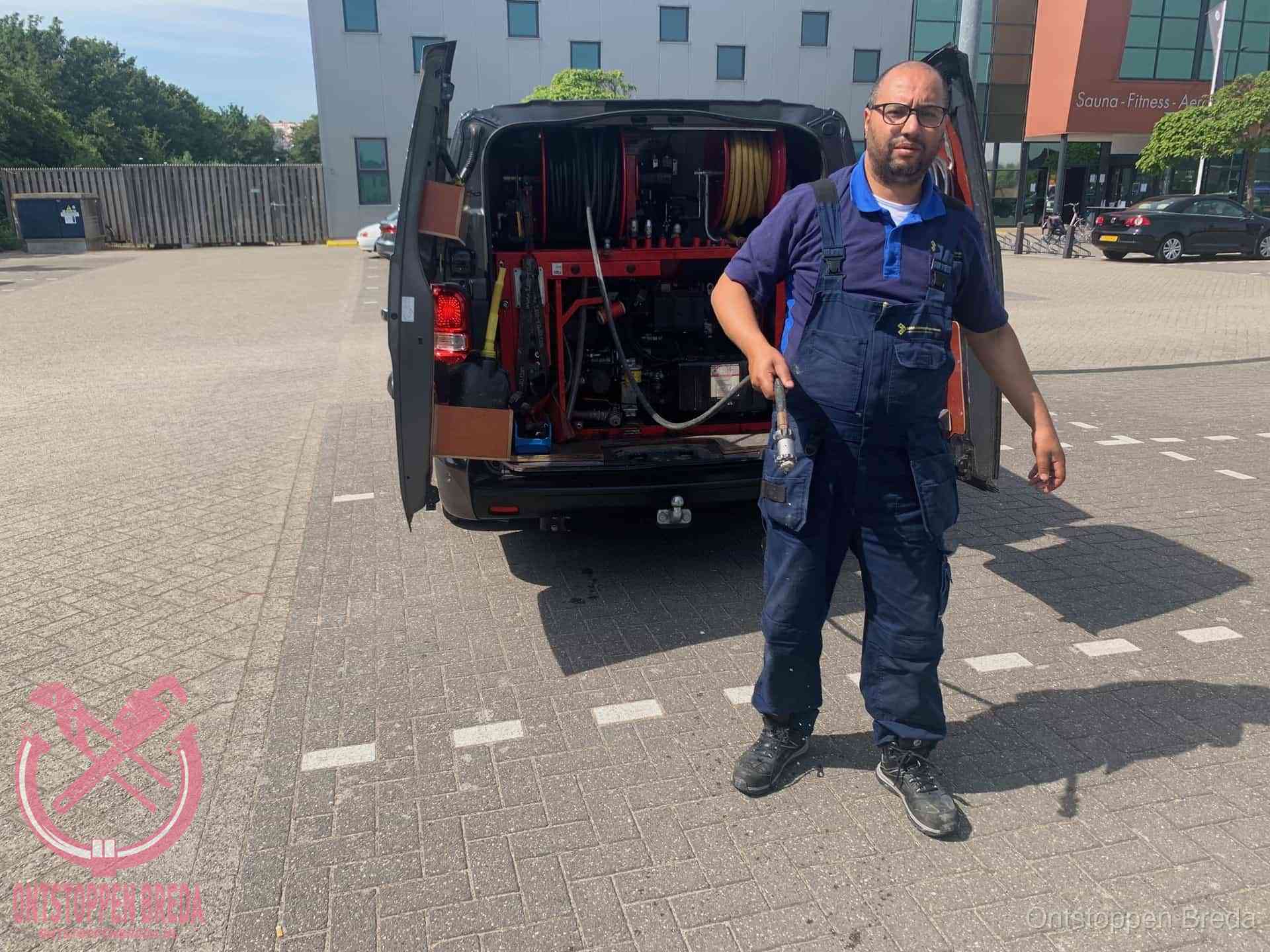 Een monteur bij zijn bestelbus met een hogedruk- en rioolreinigingsunit, klaar om de oorzaak van terugkerende wc-verstoppingen aan te pakken in Breda