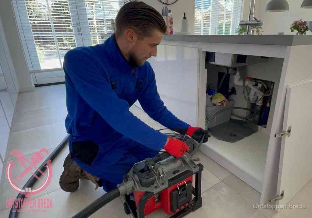 Een monteur voert een professionele elektrische ontstoppingsmachine in de afvoer onder de spoelbak tijdens het gootsteen ontstoppen in Breda Een monteur voert een professionele elektrische ontstoppingsmachine in de afvoer onder de spoelbak tijdens het gootsteen ontstoppen in Breda