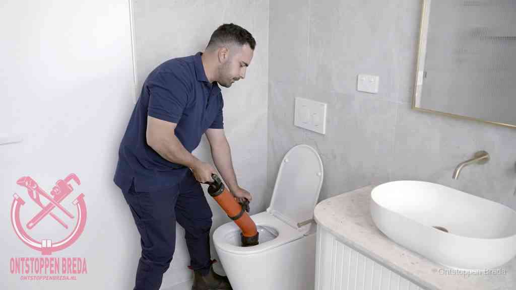 Een man gebruikt een handmatige luchtdruk-ontstopper in een modern betegeld toilet om zelf de wc te ontstoppen in Breda